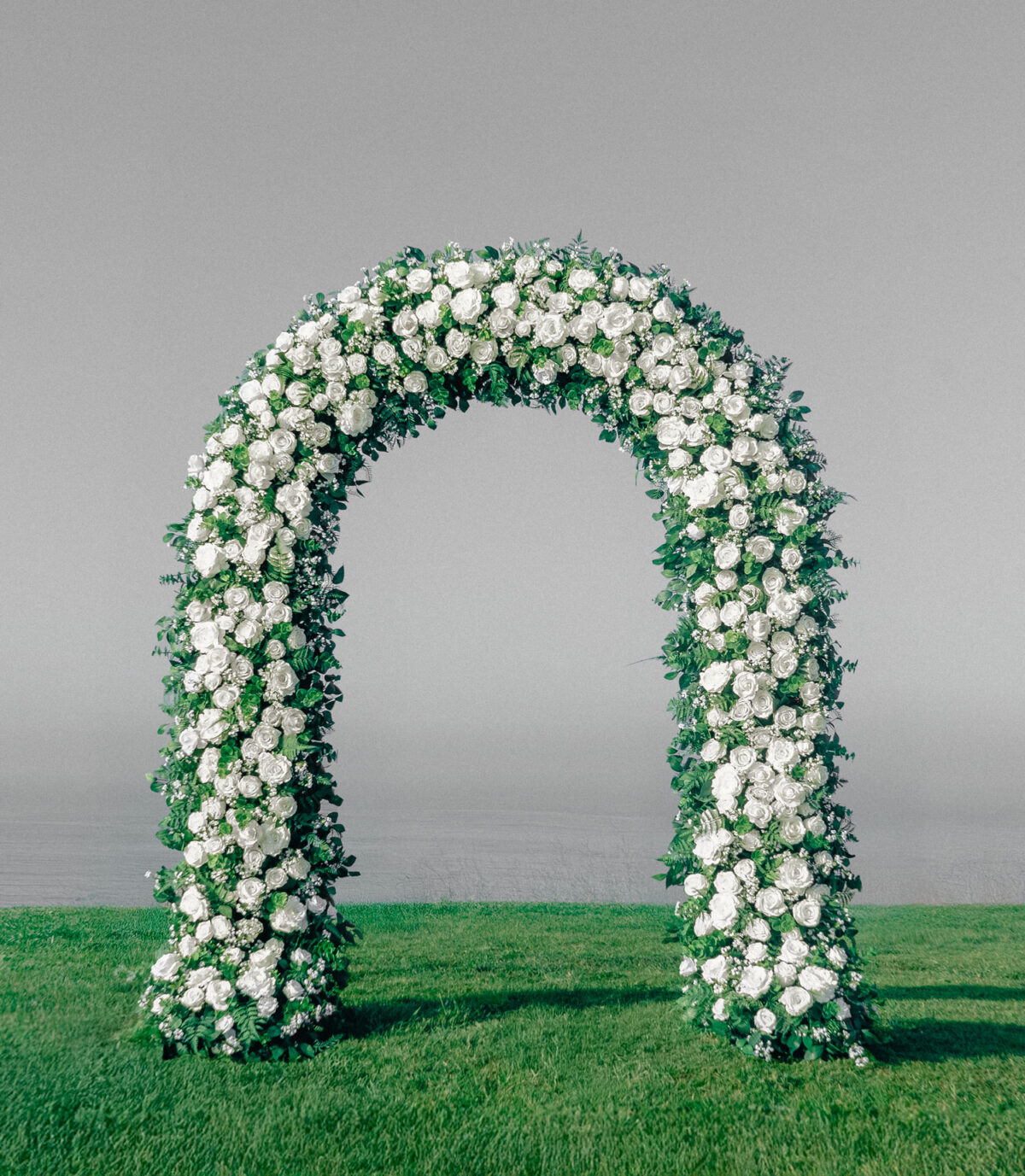 Classic white rose wedding arch with lush, symmetrical floral arrangements. A timeless and elegant backdrop, ideal for ballroom weddings or traditional church ceremonies.