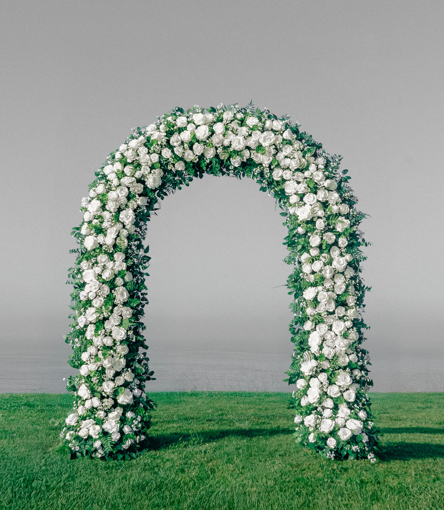 Classic white rose wedding arch with lush, symmetrical floral arrangements. A timeless and elegant backdrop, ideal for ballroom weddings or traditional church ceremonies.