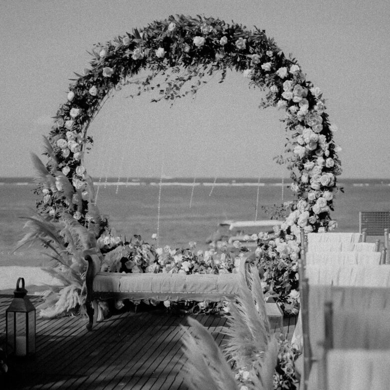 Artificial flower wedding arch at a real outdoor ceremony, framing the couple as they say their vows.